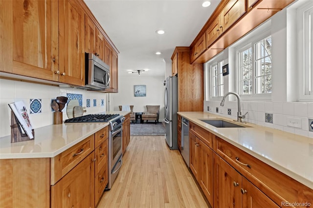 kitchen with stainless steel appliances, sink, backsplash, and light wood-type flooring