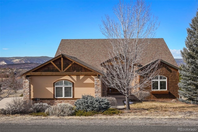 view of front of property with stone siding, roof with shingles, and a mountain view