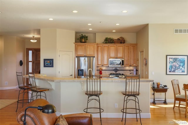 kitchen featuring visible vents, a kitchen breakfast bar, light countertops, appliances with stainless steel finishes, and backsplash