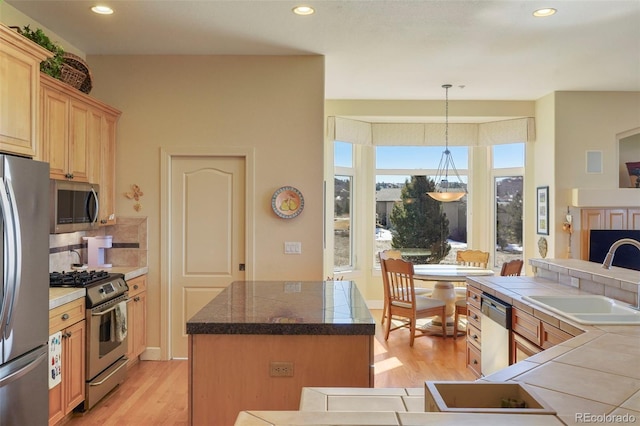 kitchen featuring a center island, light wood finished floors, light brown cabinetry, appliances with stainless steel finishes, and a sink