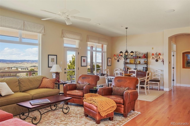 living room with arched walkways, ceiling fan, light wood-style flooring, and baseboards