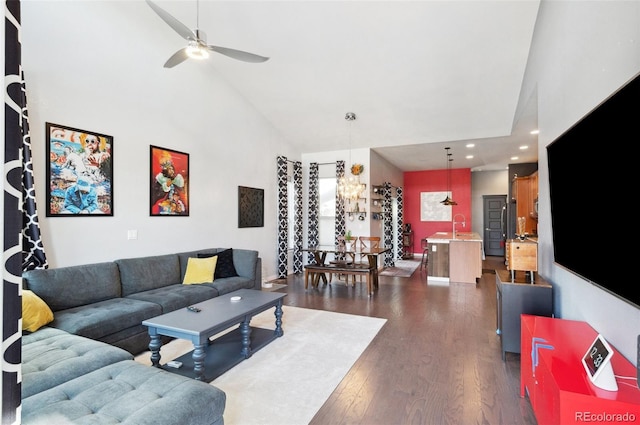 living room with sink, dark wood-type flooring, ceiling fan with notable chandelier, and high vaulted ceiling