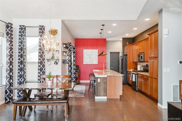 kitchen with hanging light fixtures, appliances with stainless steel finishes, light stone countertops, a kitchen bar, and an island with sink