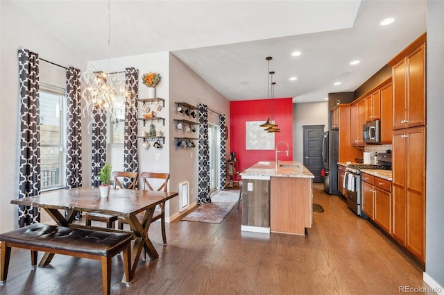 kitchen with pendant lighting, appliances with stainless steel finishes, dark wood-type flooring, a kitchen island with sink, and light stone counters