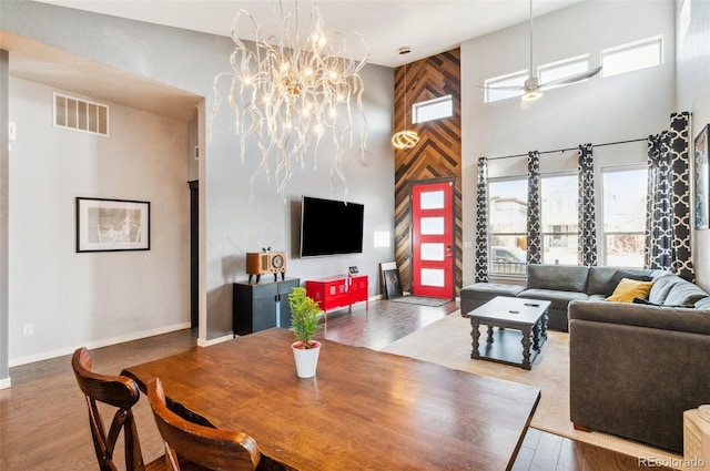 living room with ceiling fan with notable chandelier, a high ceiling, and wood-type flooring