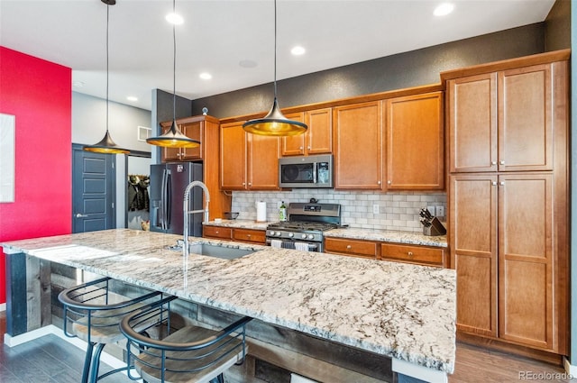 kitchen with stainless steel appliances, hanging light fixtures, an island with sink, and a kitchen breakfast bar