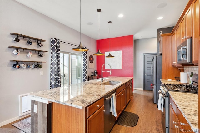 kitchen with pendant lighting, light hardwood / wood-style flooring, stainless steel appliances, sink, and a center island with sink