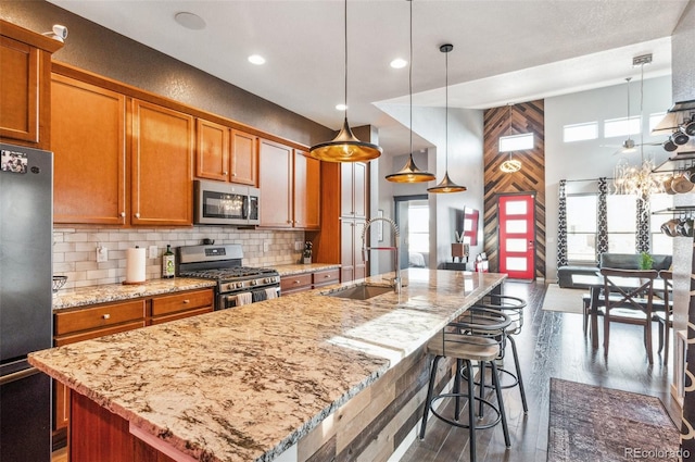 kitchen with decorative light fixtures, sink, appliances with stainless steel finishes, and an island with sink