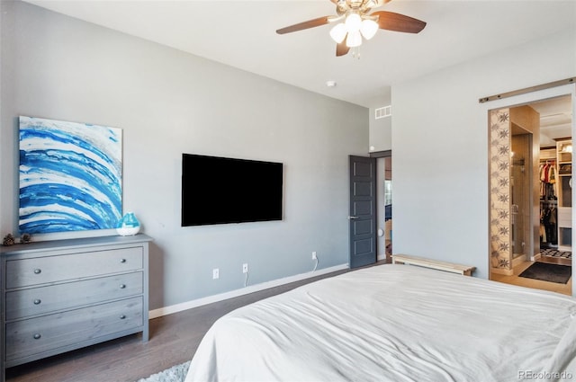 bedroom featuring a walk in closet, dark hardwood / wood-style flooring, a closet, ceiling fan, and a barn door