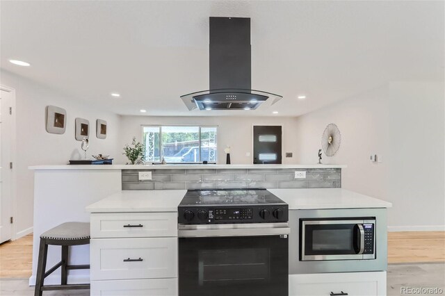 kitchen featuring appliances with stainless steel finishes, island range hood, a breakfast bar, light wood-type flooring, and white cabinetry