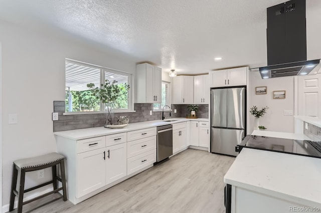 kitchen featuring appliances with stainless steel finishes, light hardwood / wood-style flooring, white cabinets, backsplash, and range hood