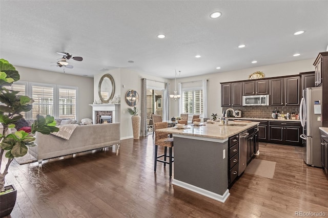 kitchen with appliances with stainless steel finishes, sink, dark hardwood / wood-style flooring, dark brown cabinetry, and a kitchen island with sink