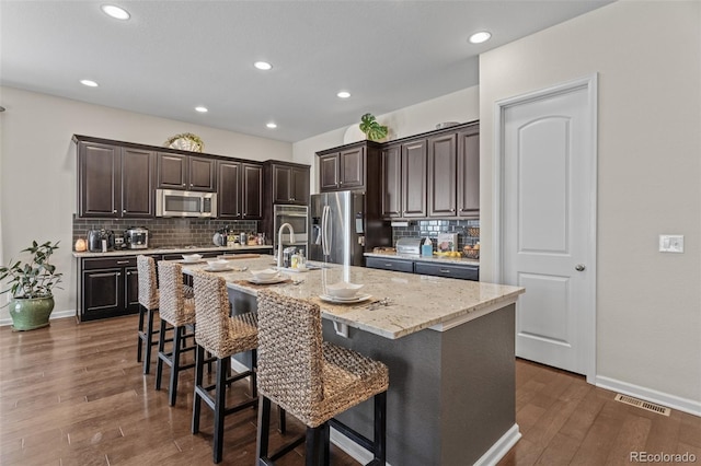 kitchen with a center island with sink, dark wood-type flooring, stainless steel appliances, and a breakfast bar