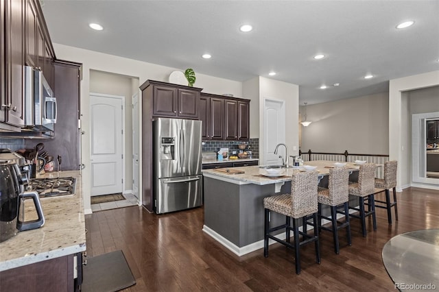 kitchen with a kitchen breakfast bar, dark hardwood / wood-style floors, stainless steel appliances, an island with sink, and light stone countertops