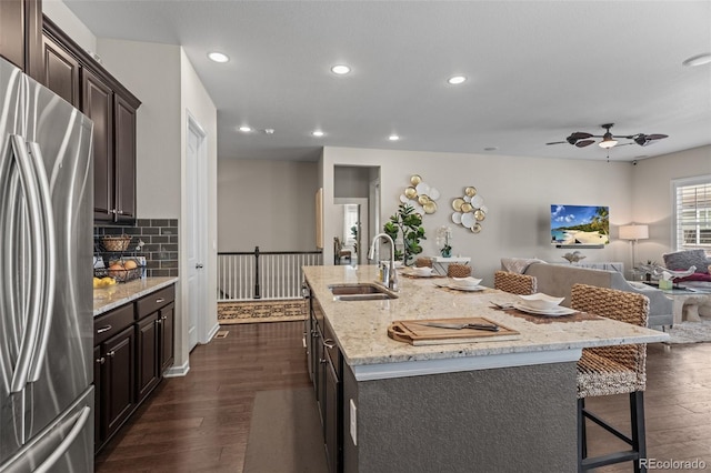 kitchen with a center island with sink, stainless steel refrigerator, sink, dark wood-type flooring, and a breakfast bar area