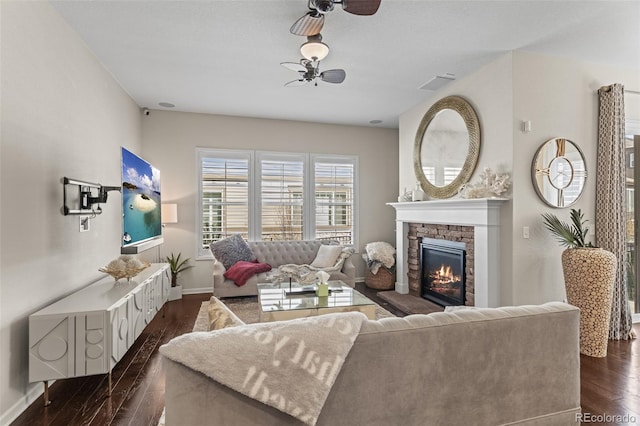 living room with ceiling fan, dark hardwood / wood-style flooring, and a stone fireplace