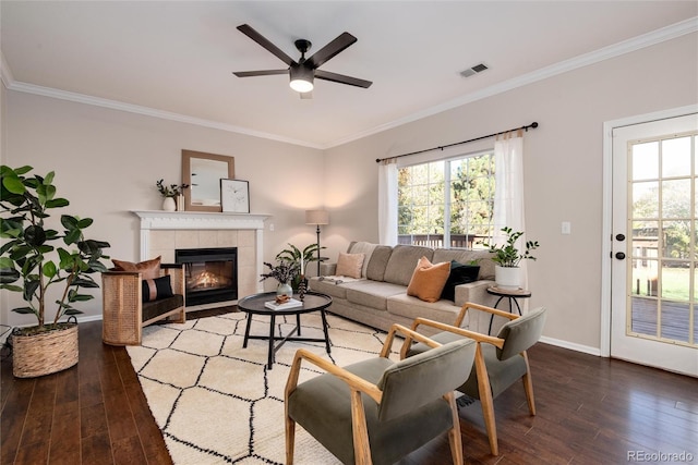 living room with ceiling fan, hardwood / wood-style floors, a tile fireplace, and crown molding