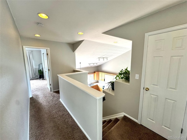 hallway featuring dark colored carpet, recessed lighting, baseboards, and an upstairs landing