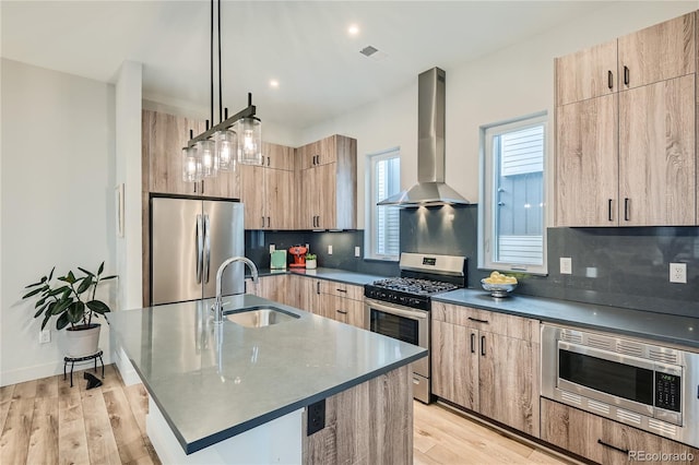 kitchen featuring sink, hanging light fixtures, wall chimney range hood, appliances with stainless steel finishes, and light wood-type flooring