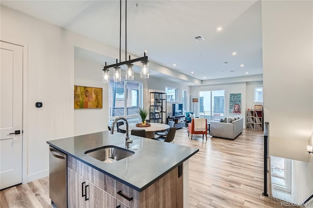 kitchen featuring pendant lighting, sink, light hardwood / wood-style flooring, stainless steel dishwasher, and an island with sink