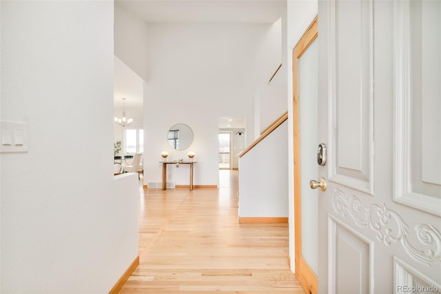 foyer featuring light wood-type flooring, a high ceiling, a notable chandelier, and baseboards