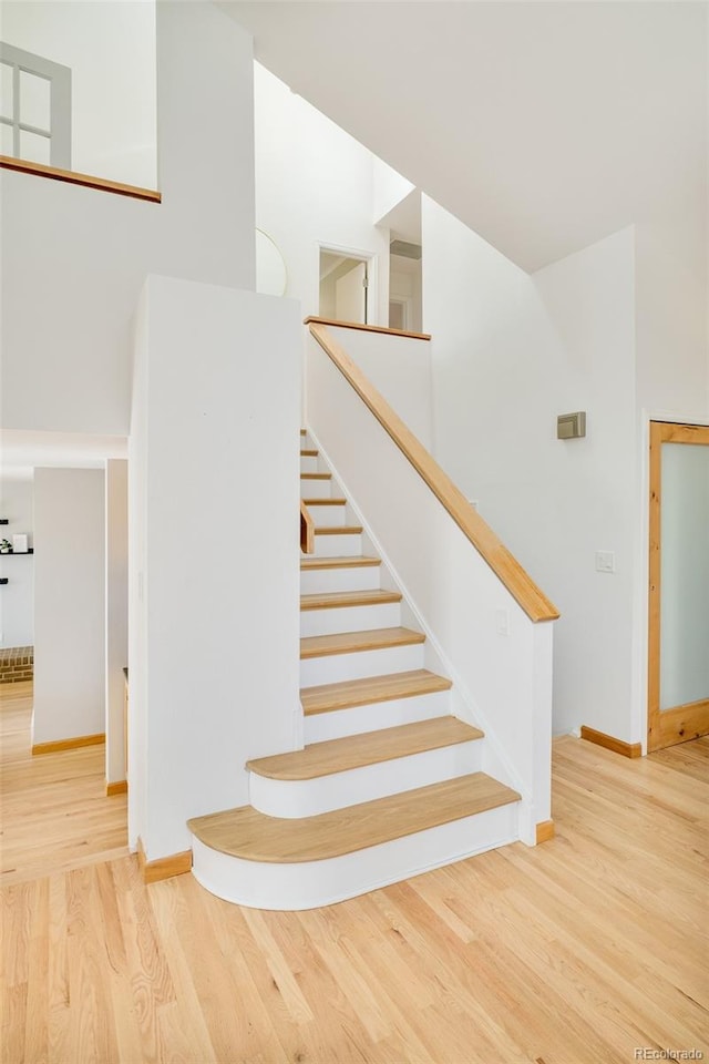 staircase with a towering ceiling, baseboards, and wood finished floors