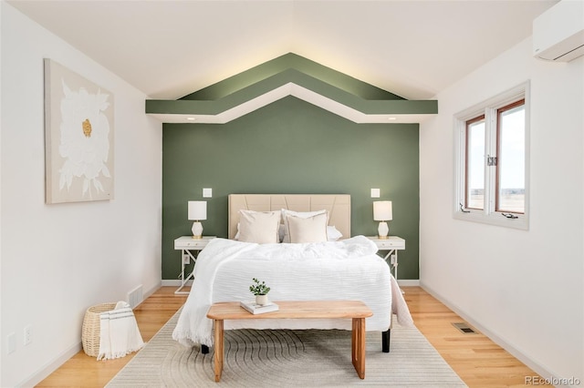 bedroom with a wall unit AC, lofted ceiling, visible vents, light wood-type flooring, and baseboards