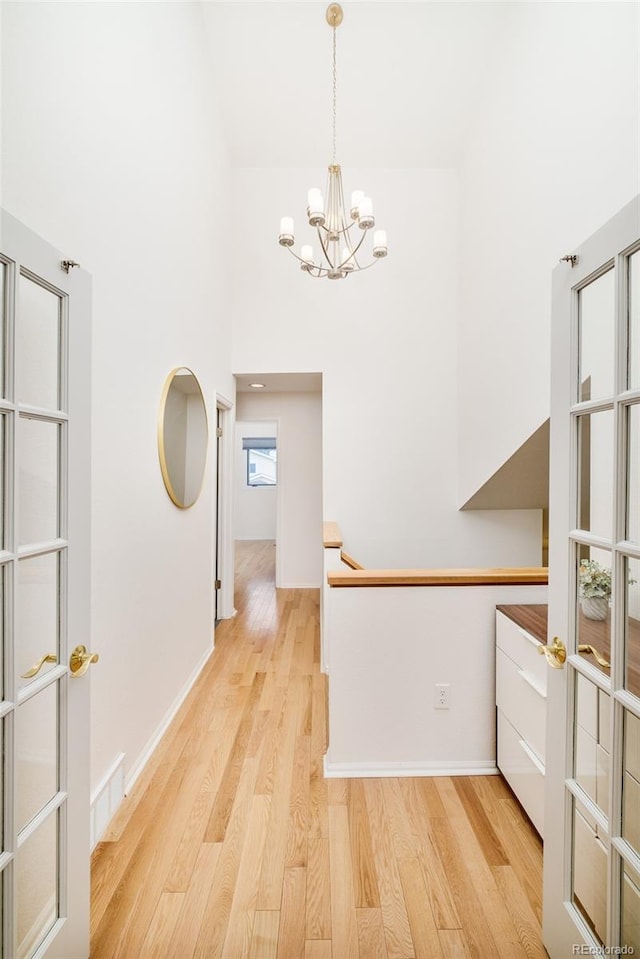 hallway featuring baseboards, a towering ceiling, visible vents, and light wood-style floors