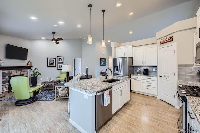 kitchen featuring stainless steel appliances, a ceiling fan, a sink, decorative backsplash, and a fireplace