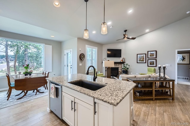 kitchen with a stone fireplace, visible vents, stainless steel dishwasher, a sink, and open floor plan