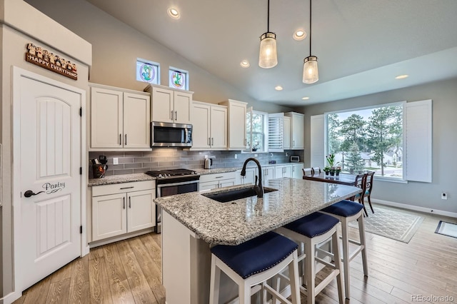 kitchen with white cabinets, stainless steel appliances, a sink, decorative backsplash, and a breakfast bar area