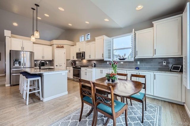 kitchen featuring stainless steel appliances, a sink, tasteful backsplash, white cabinetry, and lofted ceiling