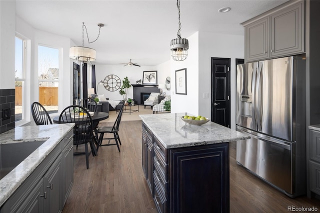 kitchen with a kitchen island, decorative light fixtures, dark hardwood / wood-style flooring, light stone counters, and stainless steel refrigerator with ice dispenser