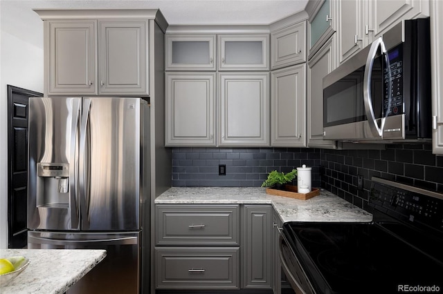 kitchen with light stone counters, decorative backsplash, gray cabinets, and appliances with stainless steel finishes