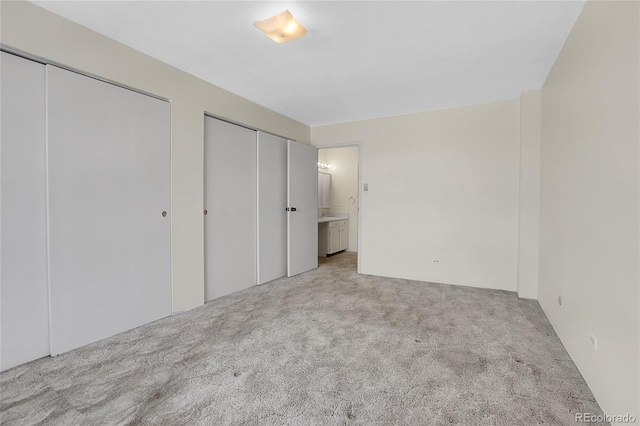 unfurnished bedroom with light colored carpet, ensuite bathroom, and two closets