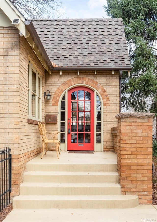 entrance to property featuring brick siding and roof with shingles