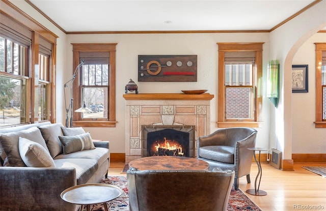 living room with wood finished floors, baseboards, arched walkways, a lit fireplace, and crown molding