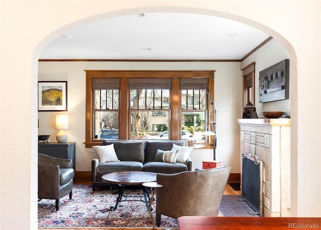 living area featuring baseboards, a fireplace with flush hearth, a healthy amount of sunlight, and ornamental molding