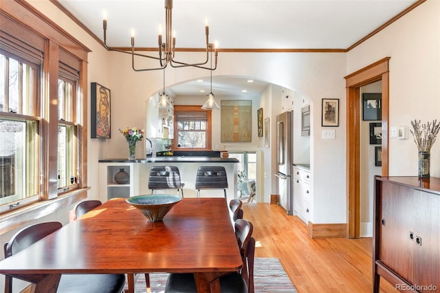 dining room with baseboards, light wood-style floors, arched walkways, and ornamental molding