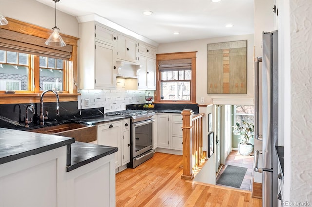 kitchen with dark countertops, tasteful backsplash, light wood-type flooring, appliances with stainless steel finishes, and a sink