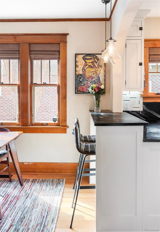 kitchen featuring wood finished floors, baseboards, pendant lighting, white cabinetry, and dark countertops