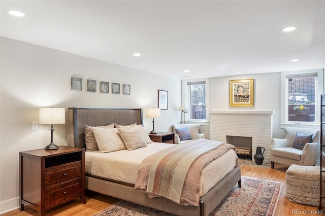 bedroom with light wood finished floors, recessed lighting, and a brick fireplace