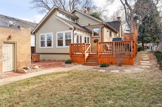 rear view of property with a lawn, a deck, a patio, roof with shingles, and a chimney