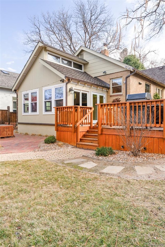 back of property with a lawn, a deck, roof with shingles, a chimney, and a patio area