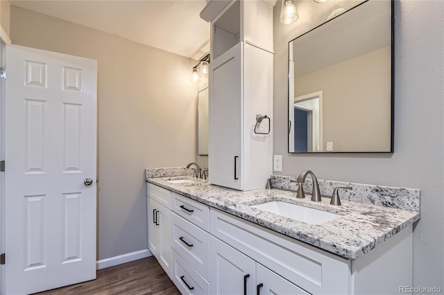 full bath featuring wood finished floors, double vanity, and baseboards