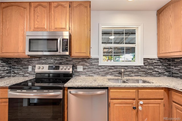 kitchen with appliances with stainless steel finishes, light stone countertops, sink, and tasteful backsplash