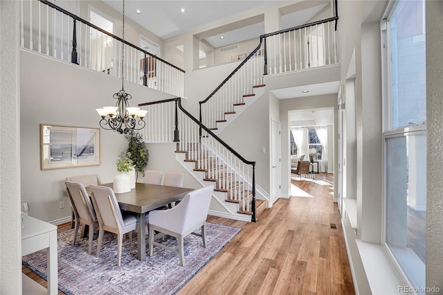 dining space featuring a towering ceiling, a chandelier, and light hardwood / wood-style flooring