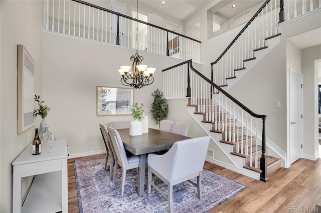 dining area with a notable chandelier, wood-type flooring, and a high ceiling