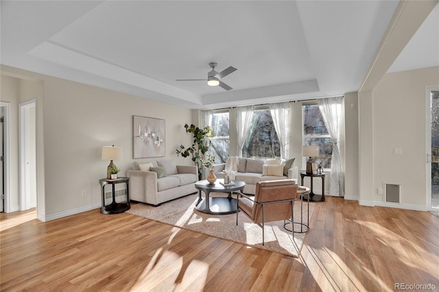 living room with ceiling fan, a tray ceiling, and light hardwood / wood-style floors