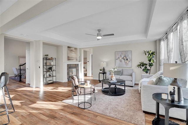 living room featuring a tile fireplace, light hardwood / wood-style flooring, ceiling fan, and a tray ceiling